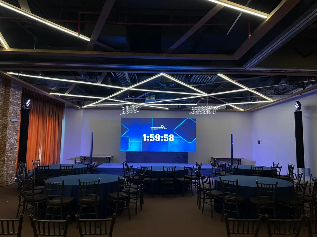 Salón universitario con pantalla LED al frente y mesas redondas