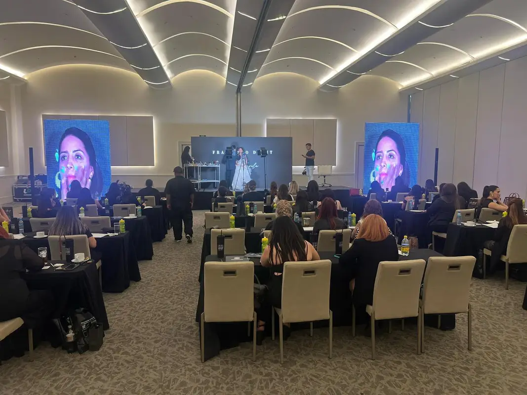 Demostración de maquillaje con dos pantallas LED verticales para el público