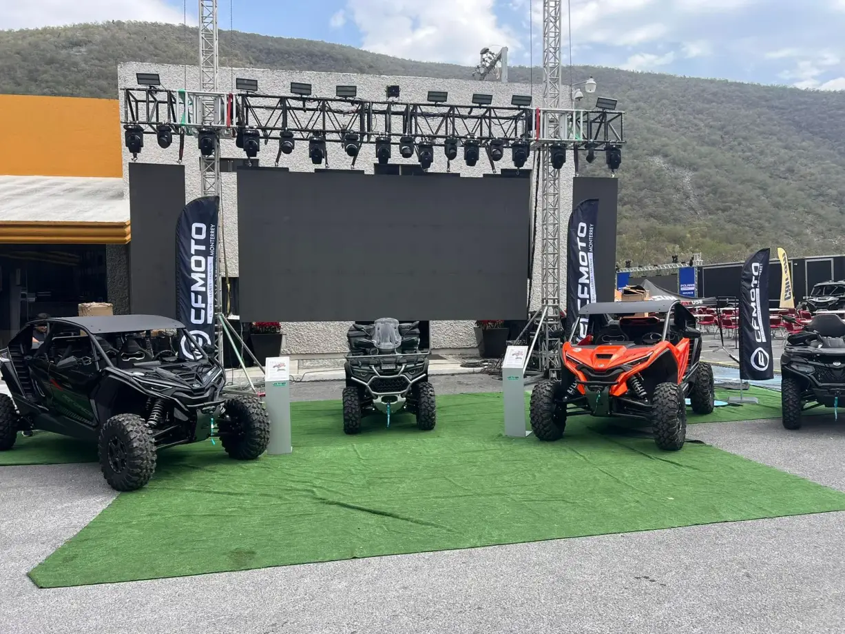 Exhibición de vehículos sobre pasto artificial frente a pantalla LED
